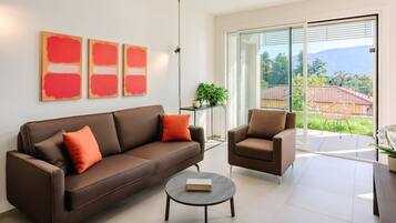 Ein modernes Wohnzimmer mit einem braunen Sofa, einem runden Couchtisch und einem braunen Sessel. An der Wand befinden sich drei abstrakte Gemälde und ein Blumentopf auf einem Tisch.