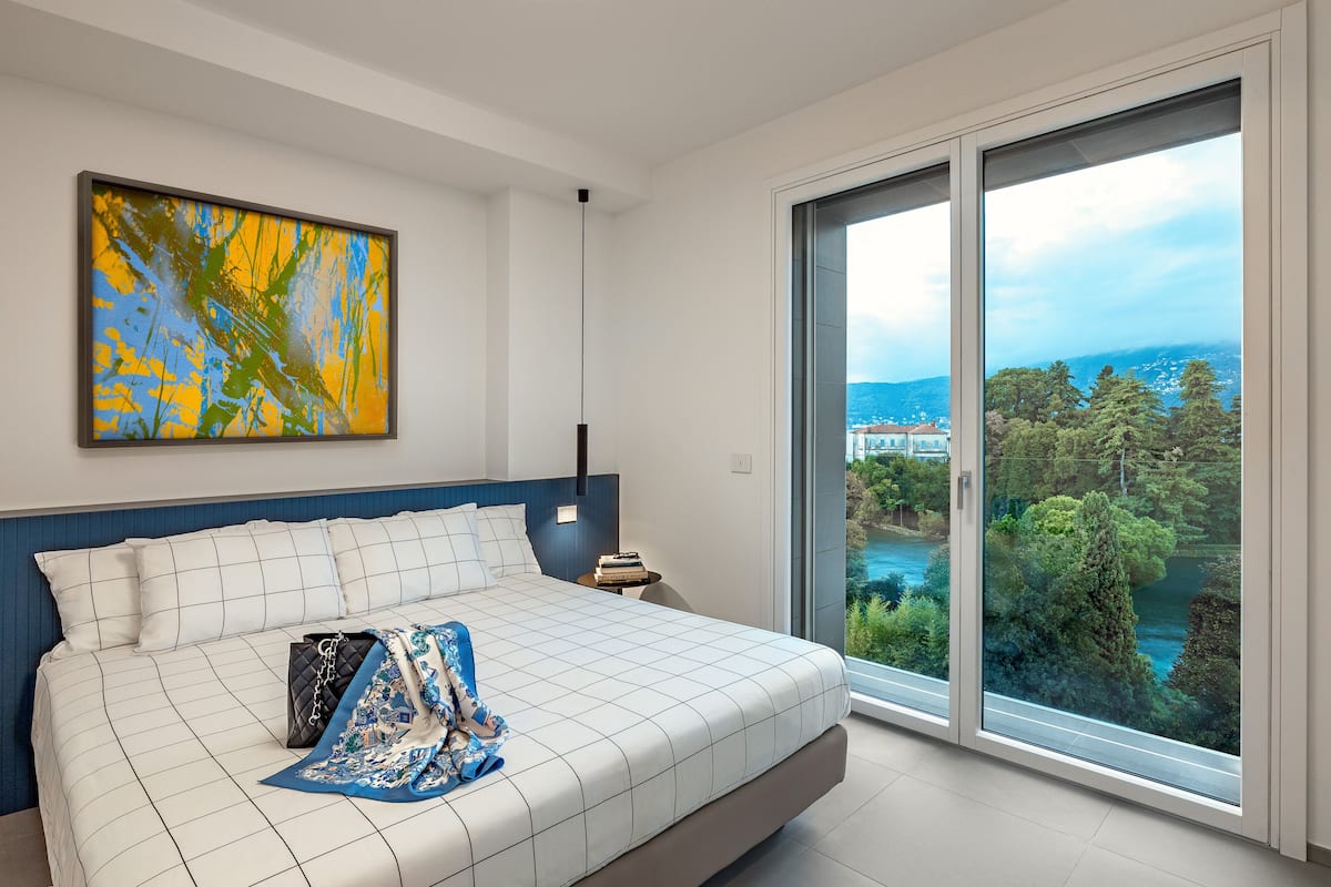 Een moderne slaapkamer met een groot bed, uitzicht op groen en een stadsgezicht door een schuifdeur.
