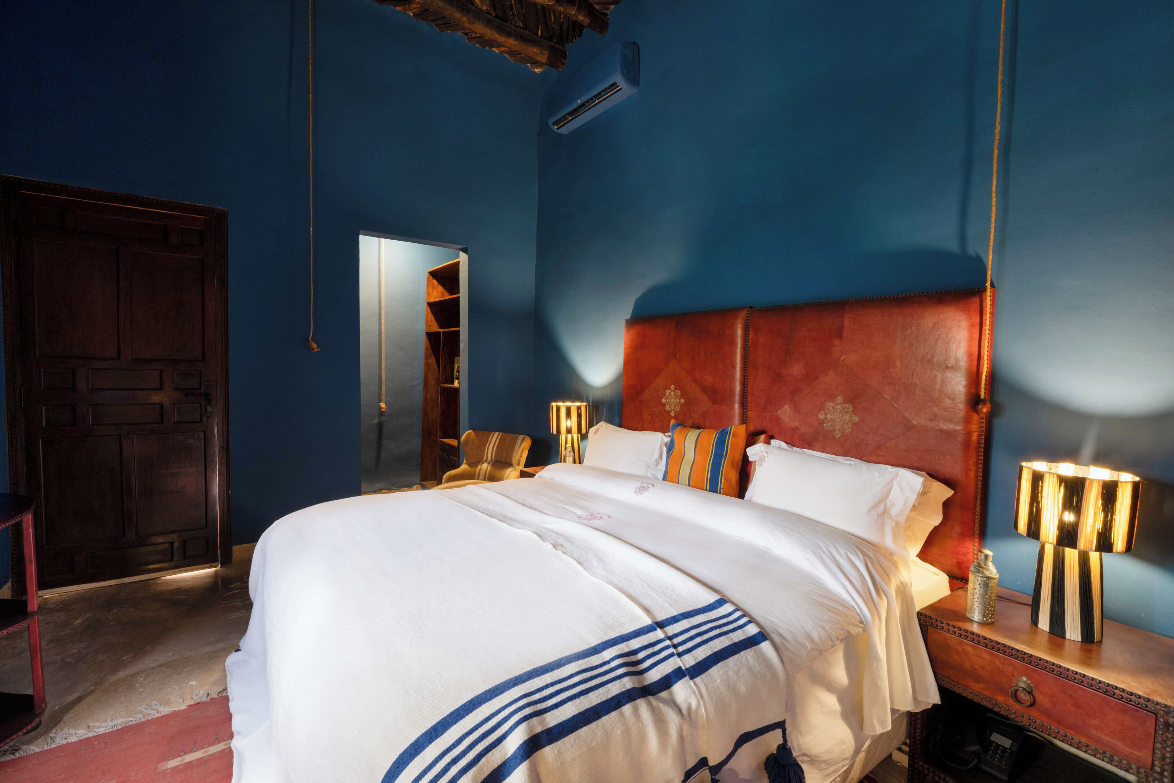 A bedroom with a large bed, a wooden headboard, a nightstand with a lamp, and a wardrobe.