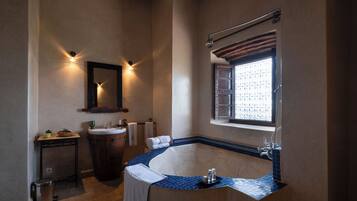 Une salle de bain avec une baignoire sur pieds, un lavabo, un miroir et une fenêtre ornée d’une grille décorative.