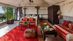 A tented room with a four-poster bed, a sofa, a dining table with a fruit bowl, and a lamp. - Kasbah Agafay Hotel And Spa (Tameslouht)