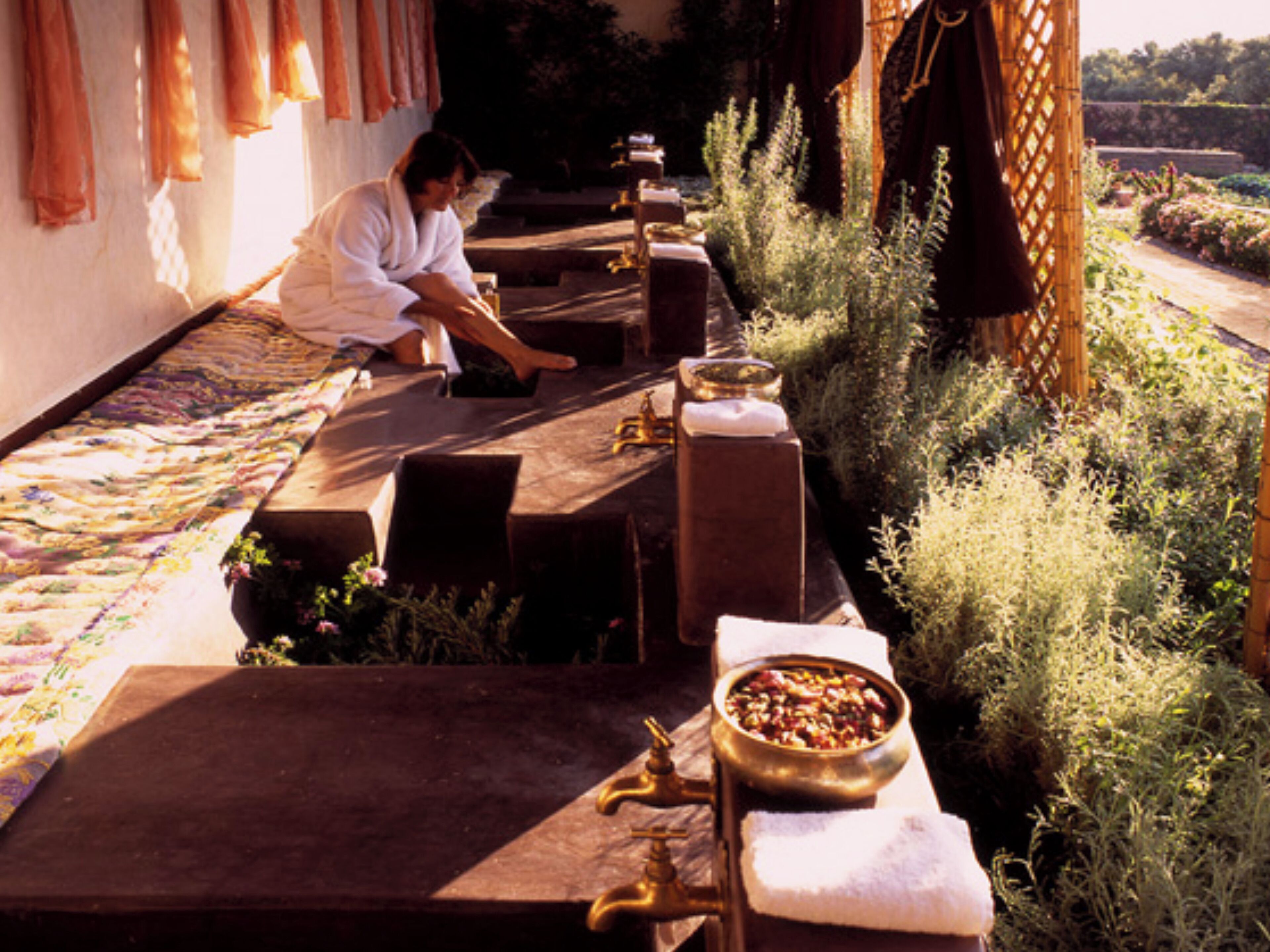 A person working at a wooden outdoor table with a bowl of food, surrounded by plants and a garden view.