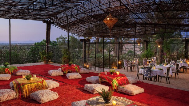 An outdoor dining area with round tables, red carpets, and white cushions. - Kasbah Agafay Hotel And Spa (Tameslouht)