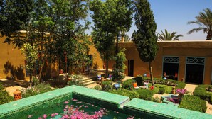 A pool with a tiled edge, surrounded by greenery and a building with a beige facade. - Kasbah Agafay Hotel And Spa (Tameslouht)