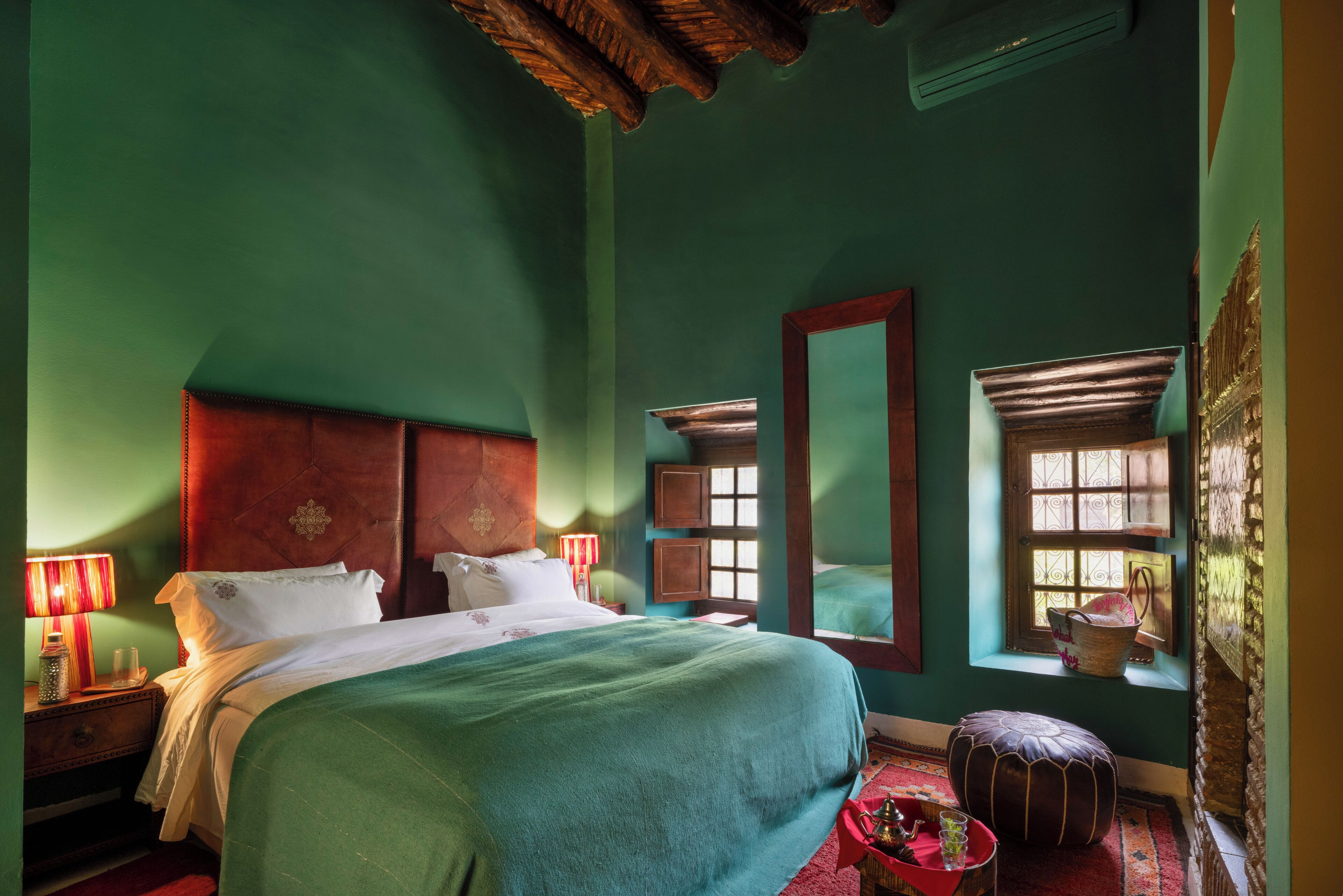 A room with a large bed, a wooden headboard, a window with a view, and a red lamp on a nightstand.