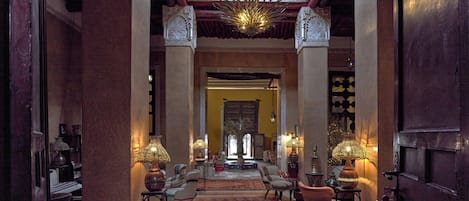 Un pasillo con columnas ornamentadas, alfombras estampadas y lámparas tradicionales.