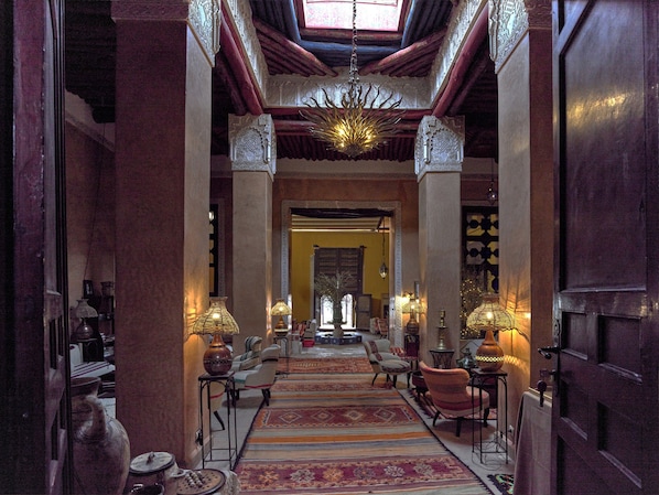 Un pasillo con columnas ornamentadas, alfombras estampadas y lámparas tradicionales.