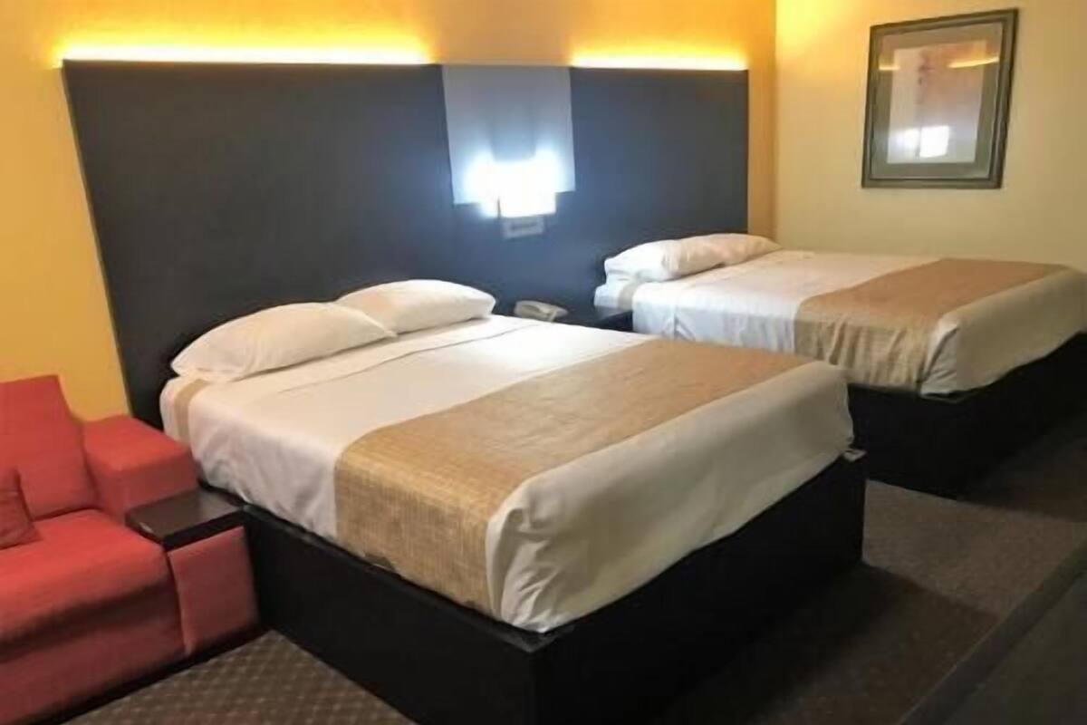 Une chambre d’hôtel avec deux lits, une chaise rouge et une table de chevet.