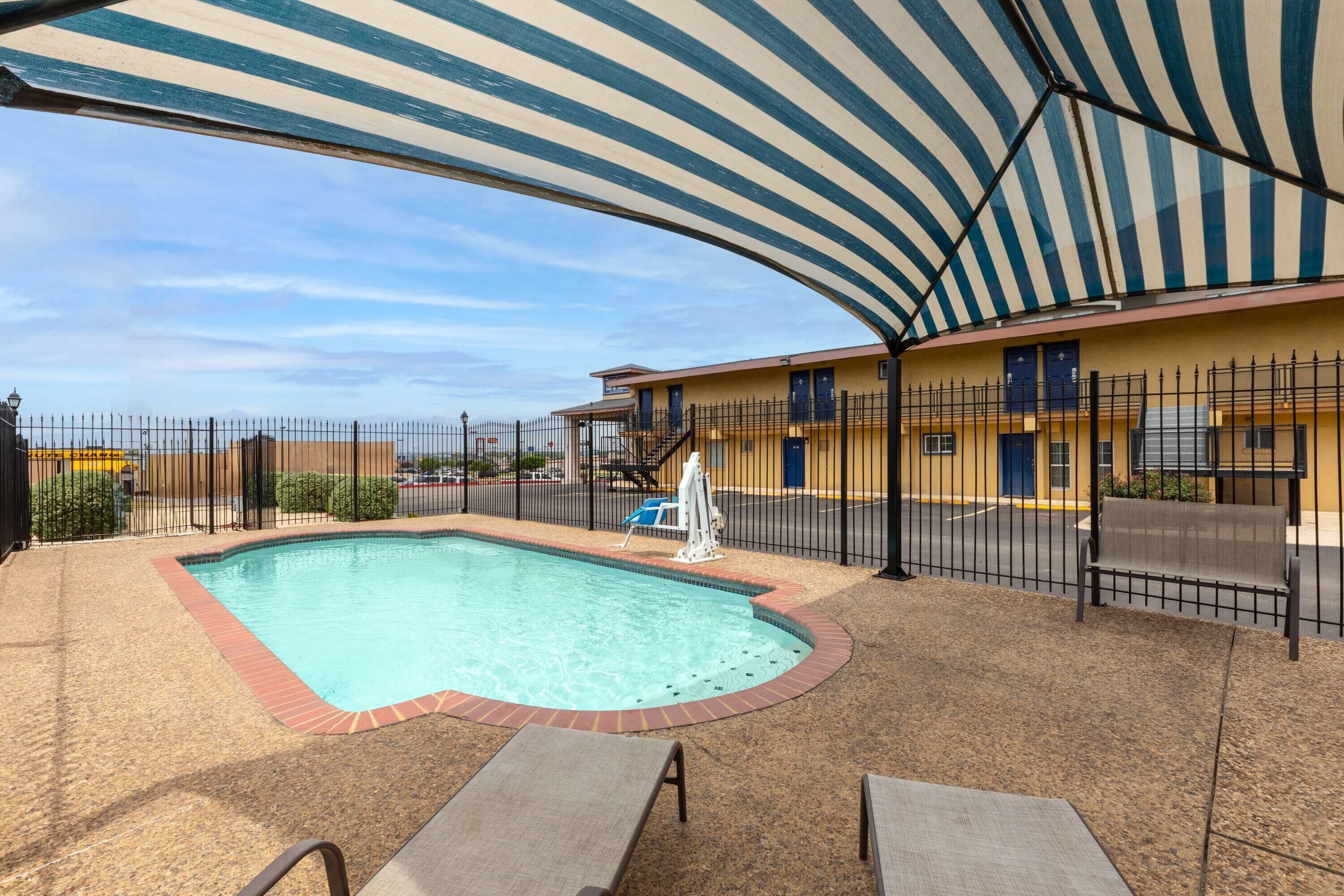 A pool area with lounge chairs, a covered seating area, and a building with multiple doors and windows.