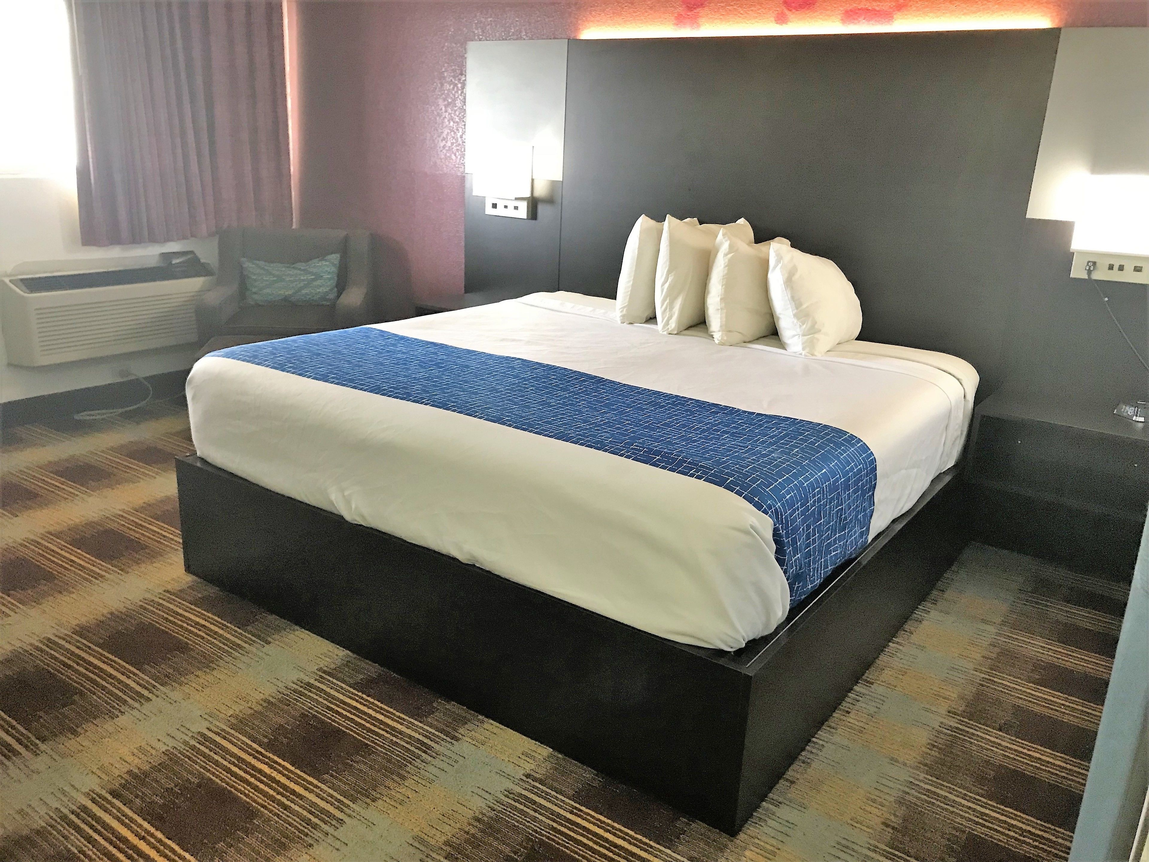 A hotel room with a large bed, a flat-screen TV, and a wall-mounted air conditioning unit.
