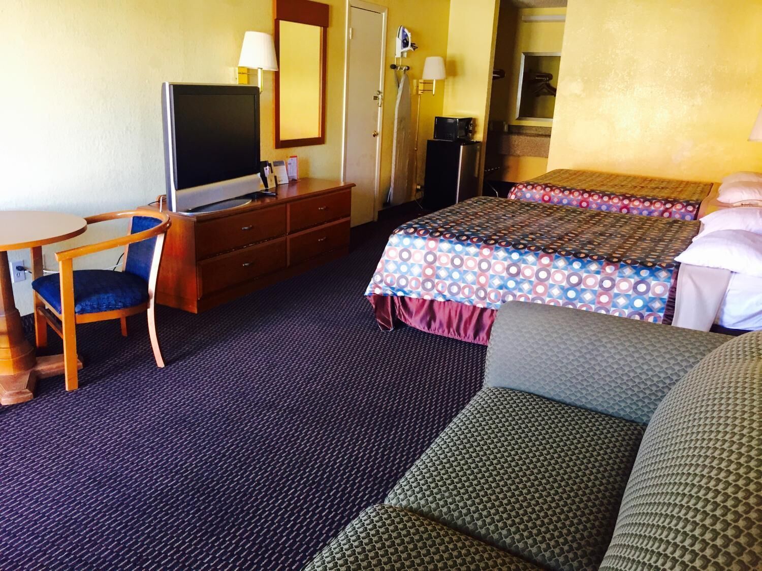 Una habitación de hotel con cama, escritorio, silla, televisor, cómoda y espejo.