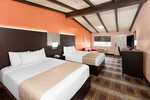 Ein Hotelzimmer mit zwei Betten, einem Schreibtisch, einem Fernseher und einem Fenster.