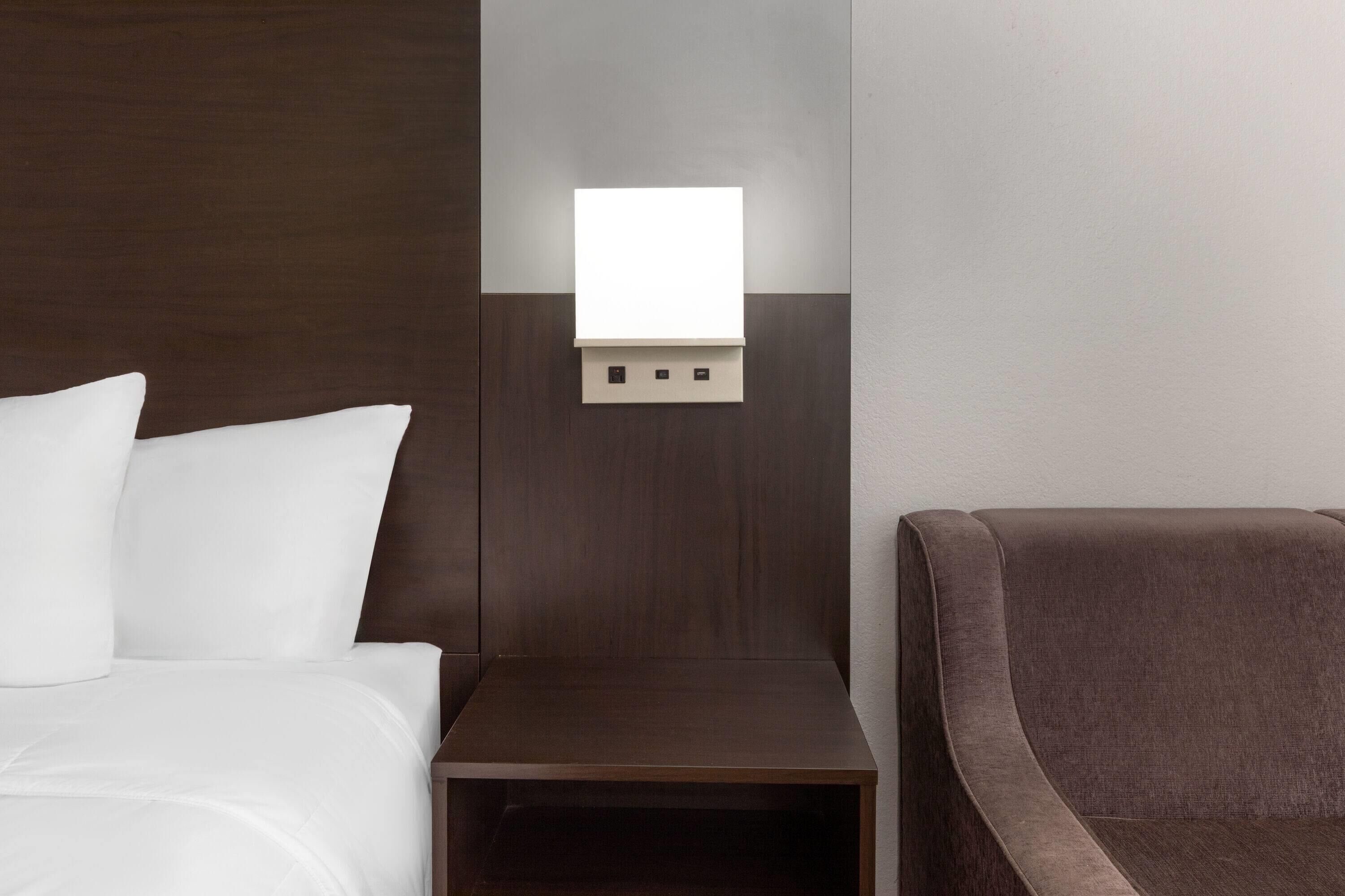 A hotel room with a bed, a nightstand, and a chair.
