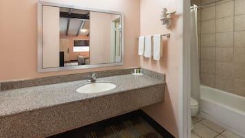 A bathroom with a granite countertop sink, a large mirror, a shower, and a toilet.