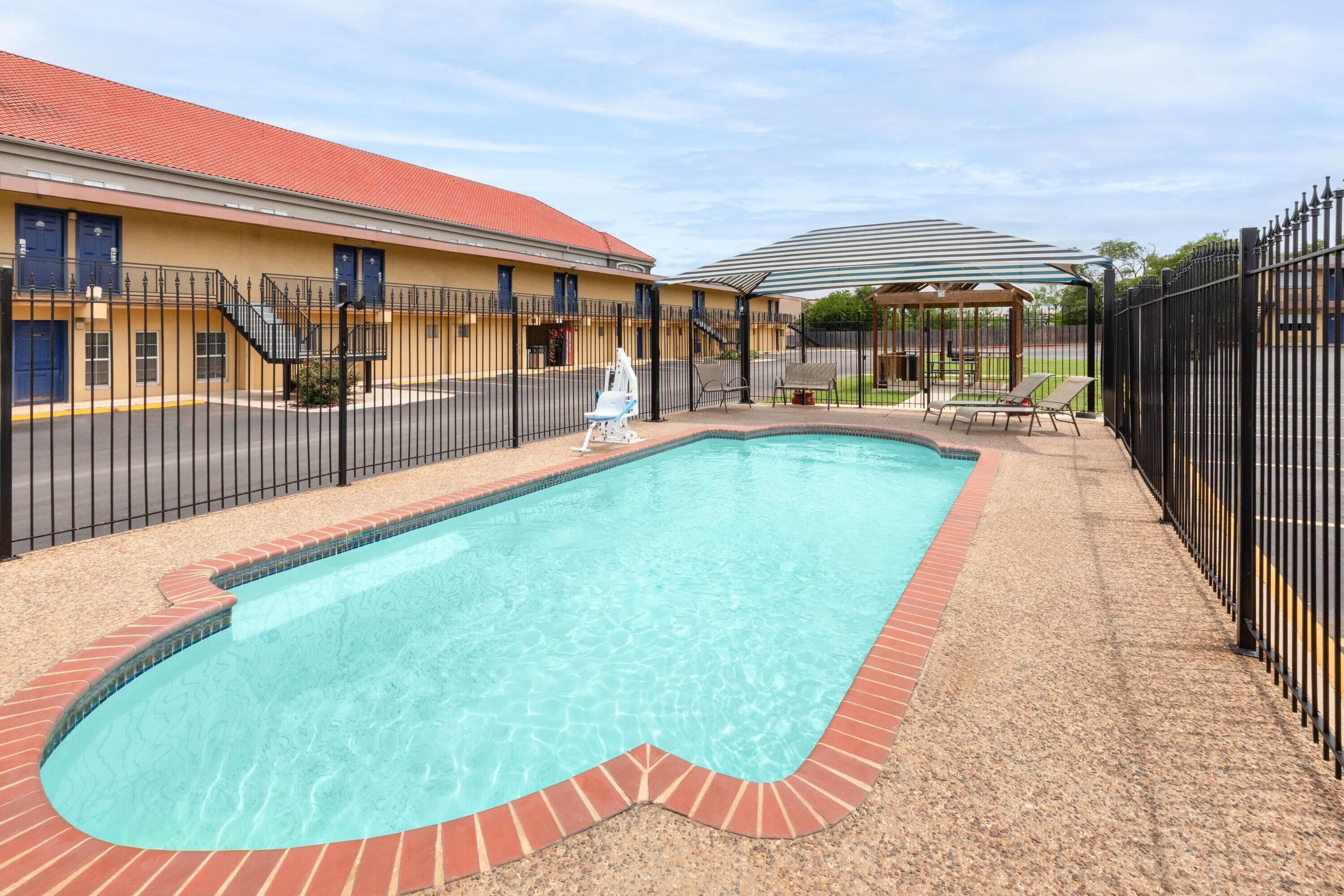 A swimming pool with a brick border, a covered seating area, and a fenced patio.