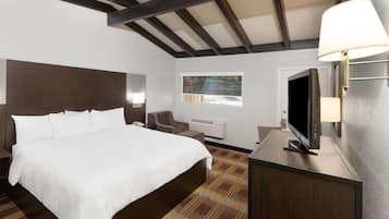Quarto de hotel com uma cama grande, uma escrivaninha com televisão de tela plana, uma cadeira, uma janela com vista e teto com vigas aparentes.