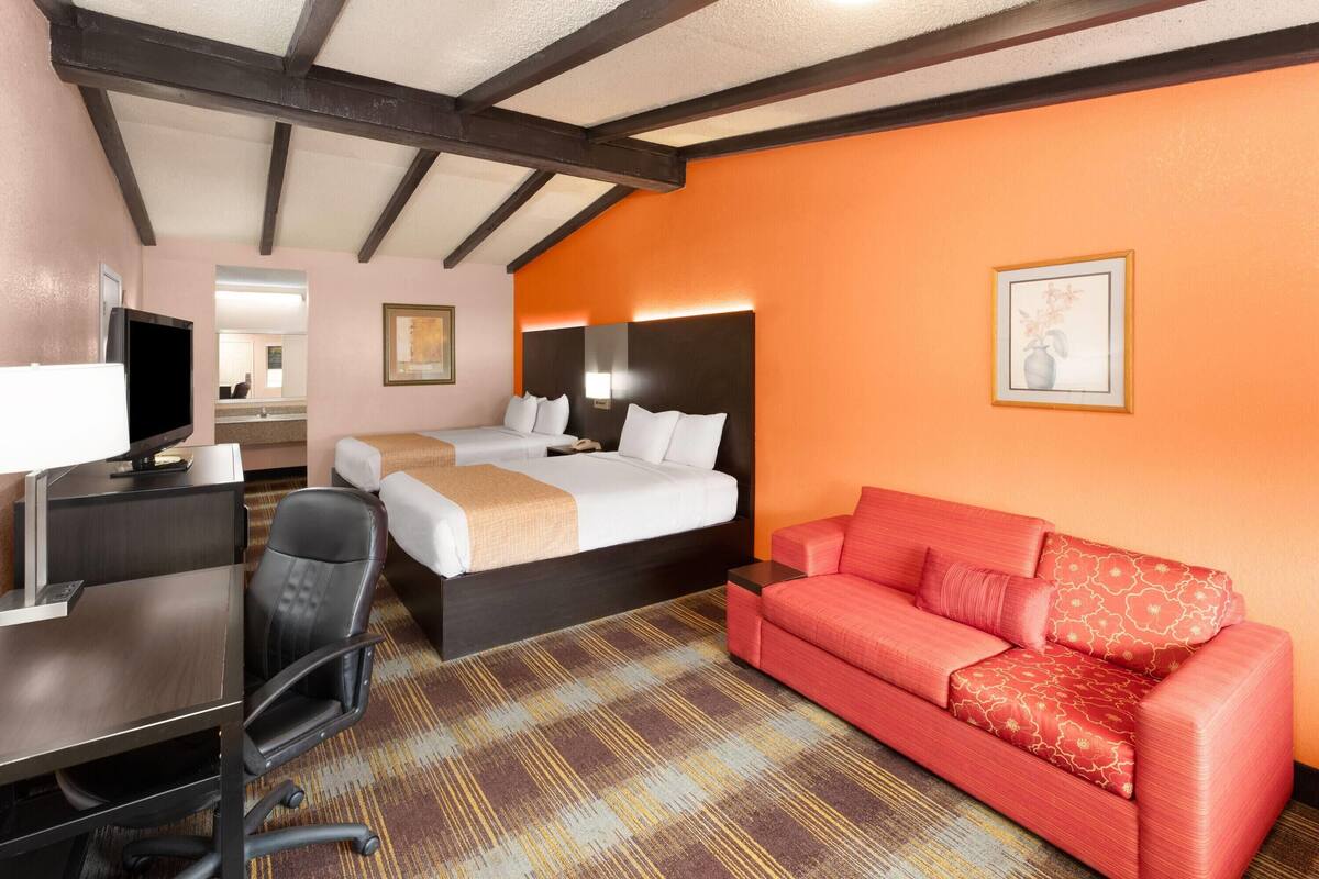 Une chambre d’hôtel avec un lit, un canapé rouge, un bureau avec un ordinateur et une télévision.