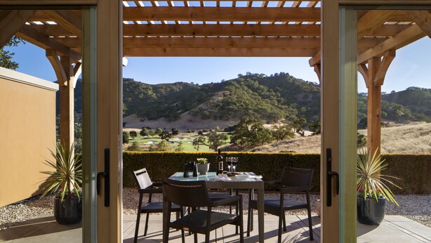 Un patio al aire libre con una mesa lista para dos personas, con vista a un paisaje montañoso.