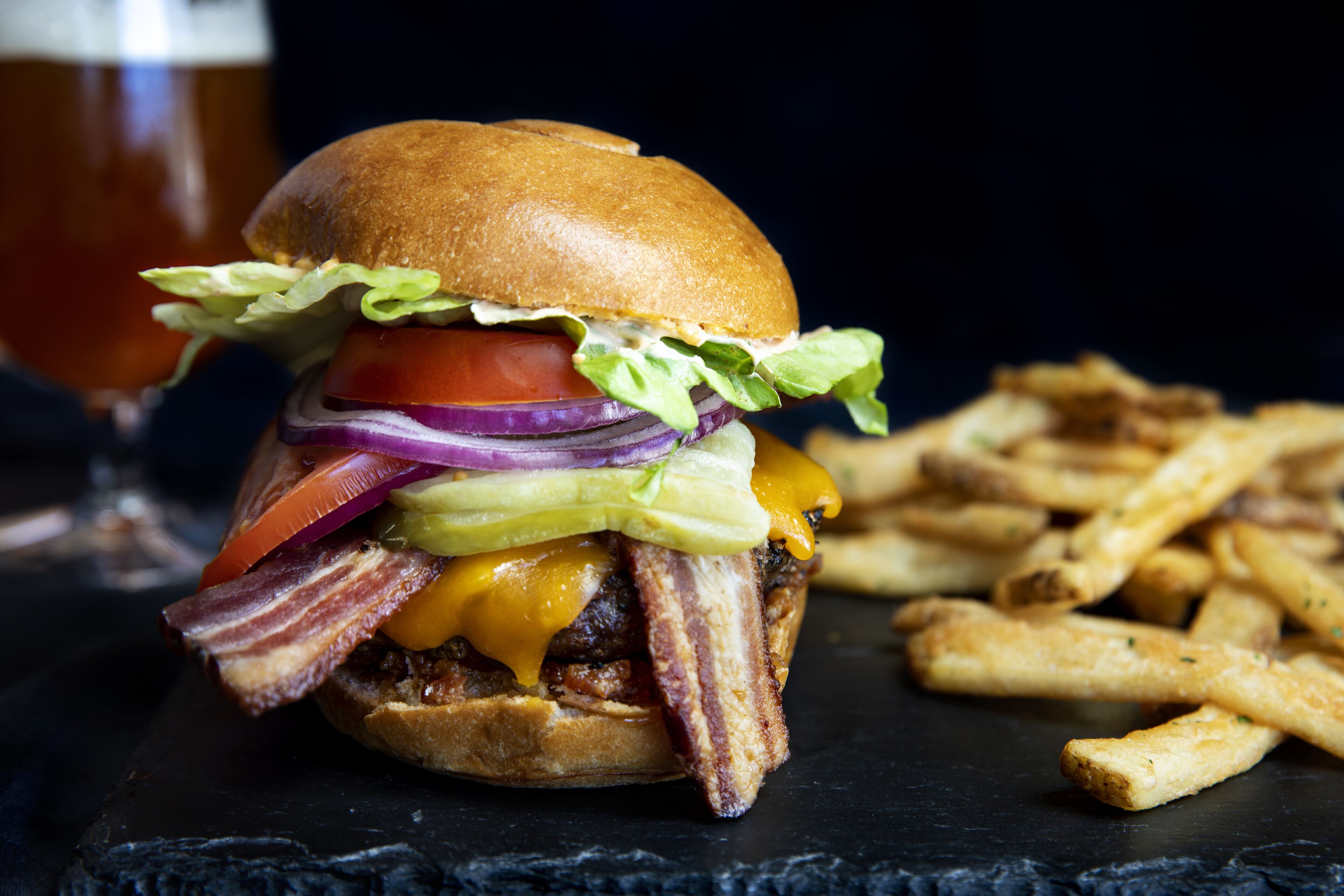 Hamburguesa con tocino, queso, lechuga, tomate y cebolla, acompañada de papas fritas.
