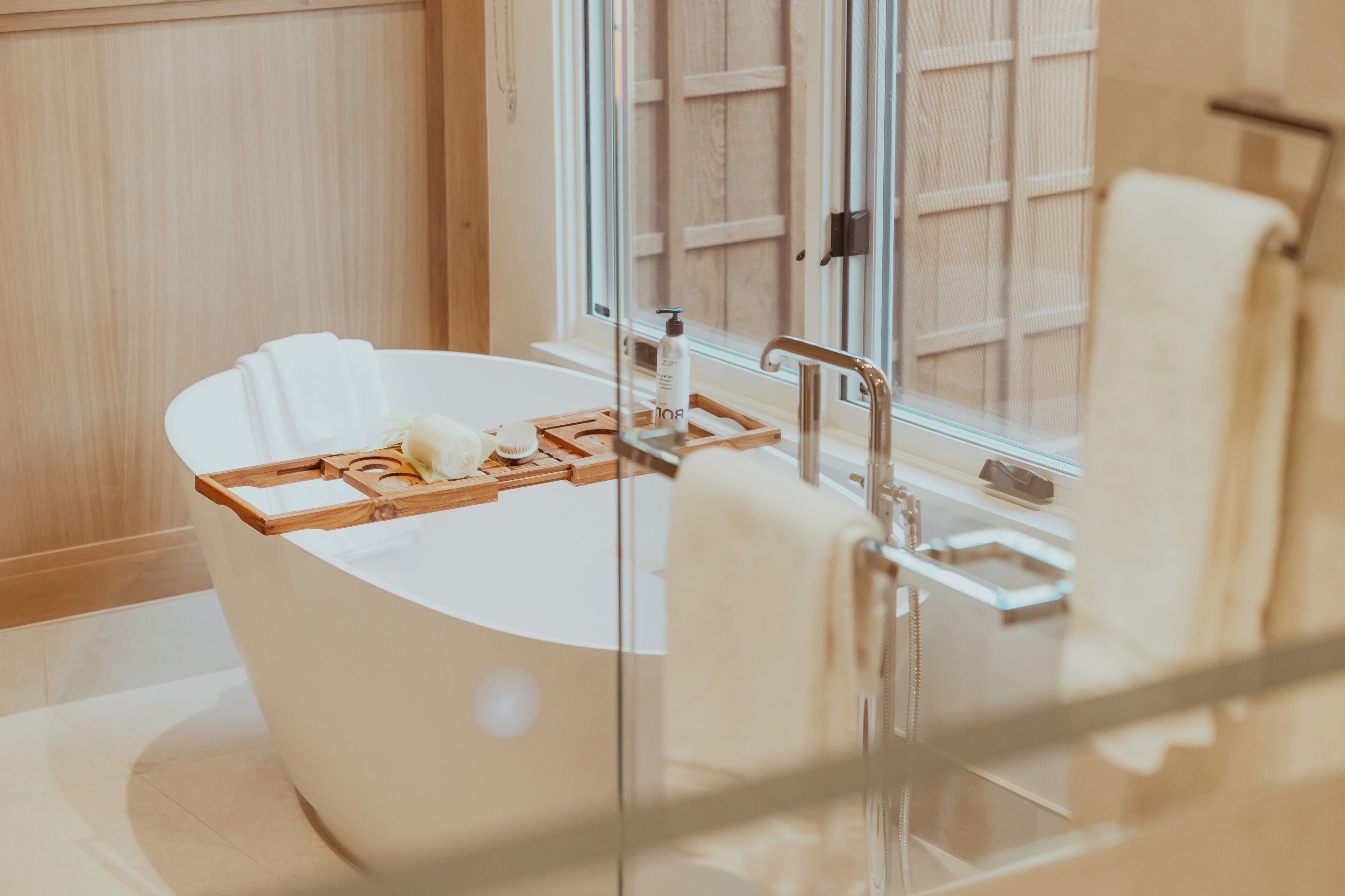 A modern bathroom with a freestanding bathtub, wooden tray, and a glass shower enclosure.