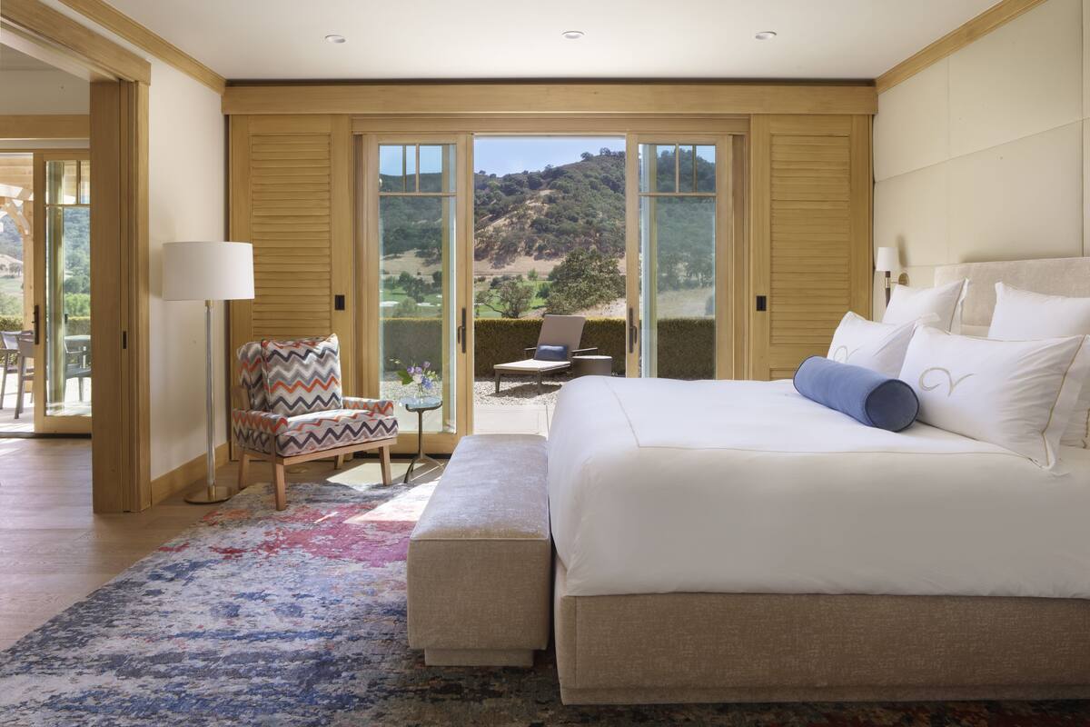 Quarto com uma cama grande, uma cadeira, uma mesa e vista para uma encosta.