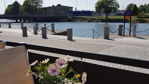 A wooden table with a potted plant, a chair, and a view of a river with a bridge and a building in the background.