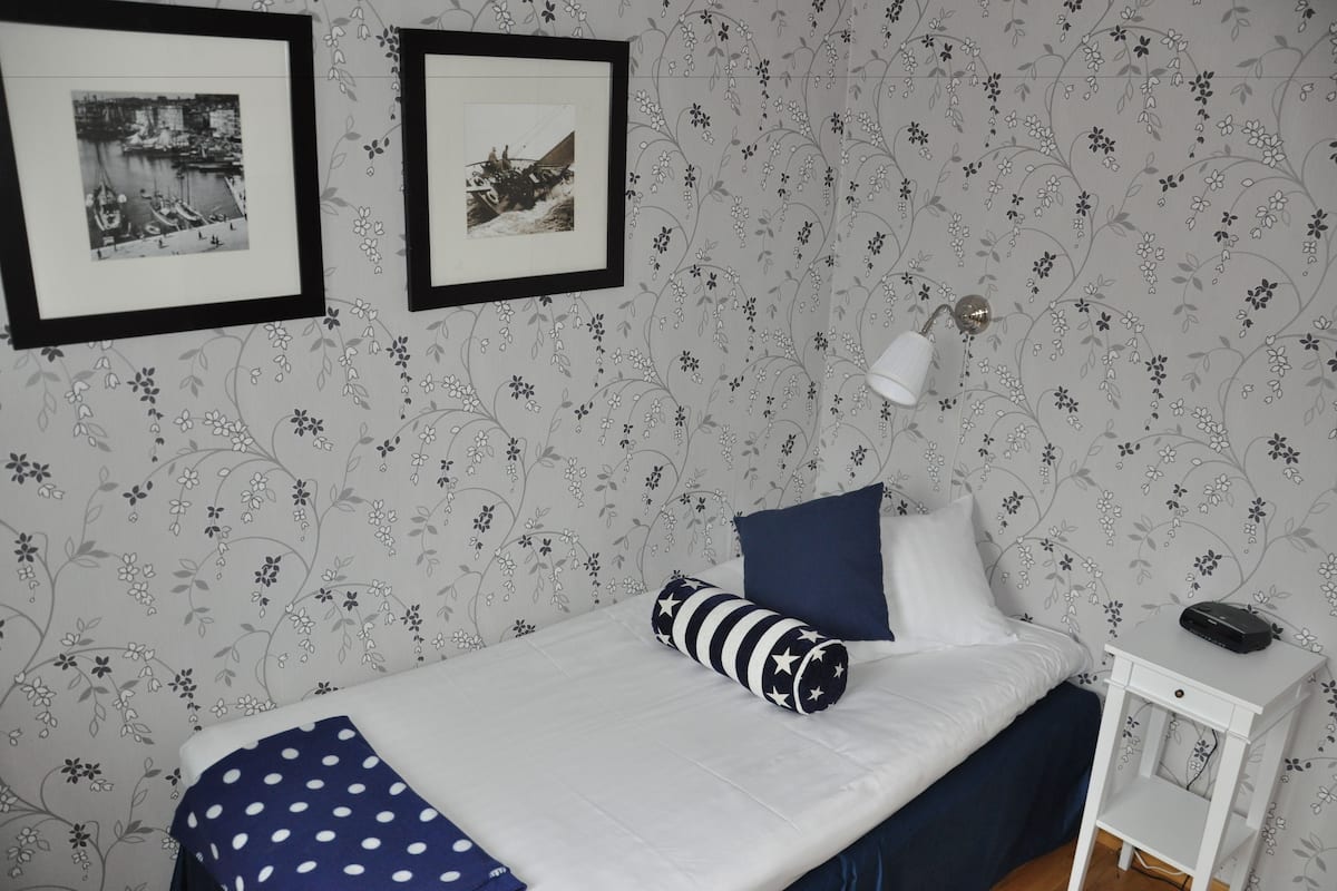 Une chambre à coucher avec un lit, un oreiller, une lampe, une table de chevet et deux tableaux encadrés accrochés au mur.