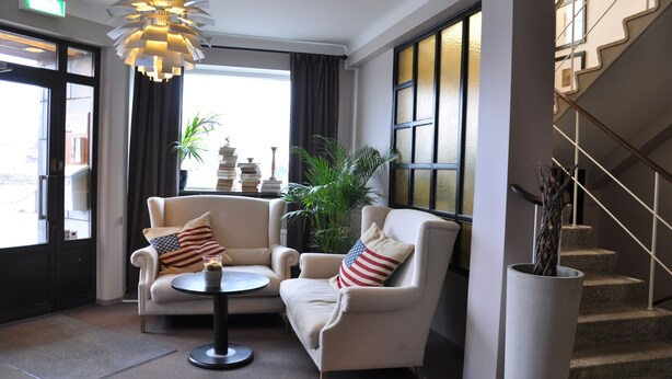 A hotel lobby with two armchairs, a small table, a potted plant, and a staircase.