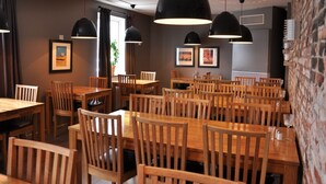 A restaurant with wooden tables and chairs, black pendant lights, and framed pictures on the walls.