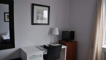 A hotel room with a desk, chair, television, and a mirror.