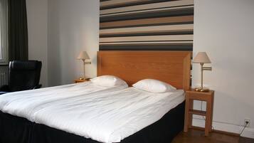 Una cama bien hecha con sábanas blancas y dos almohadas, un cabecero de madera, dos lámparas de noche y una silla negra.
