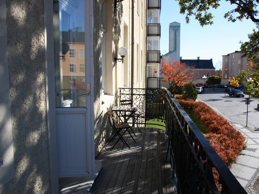 Een houten terras met een metalen hekwerk, een tafel en twee stoelen.