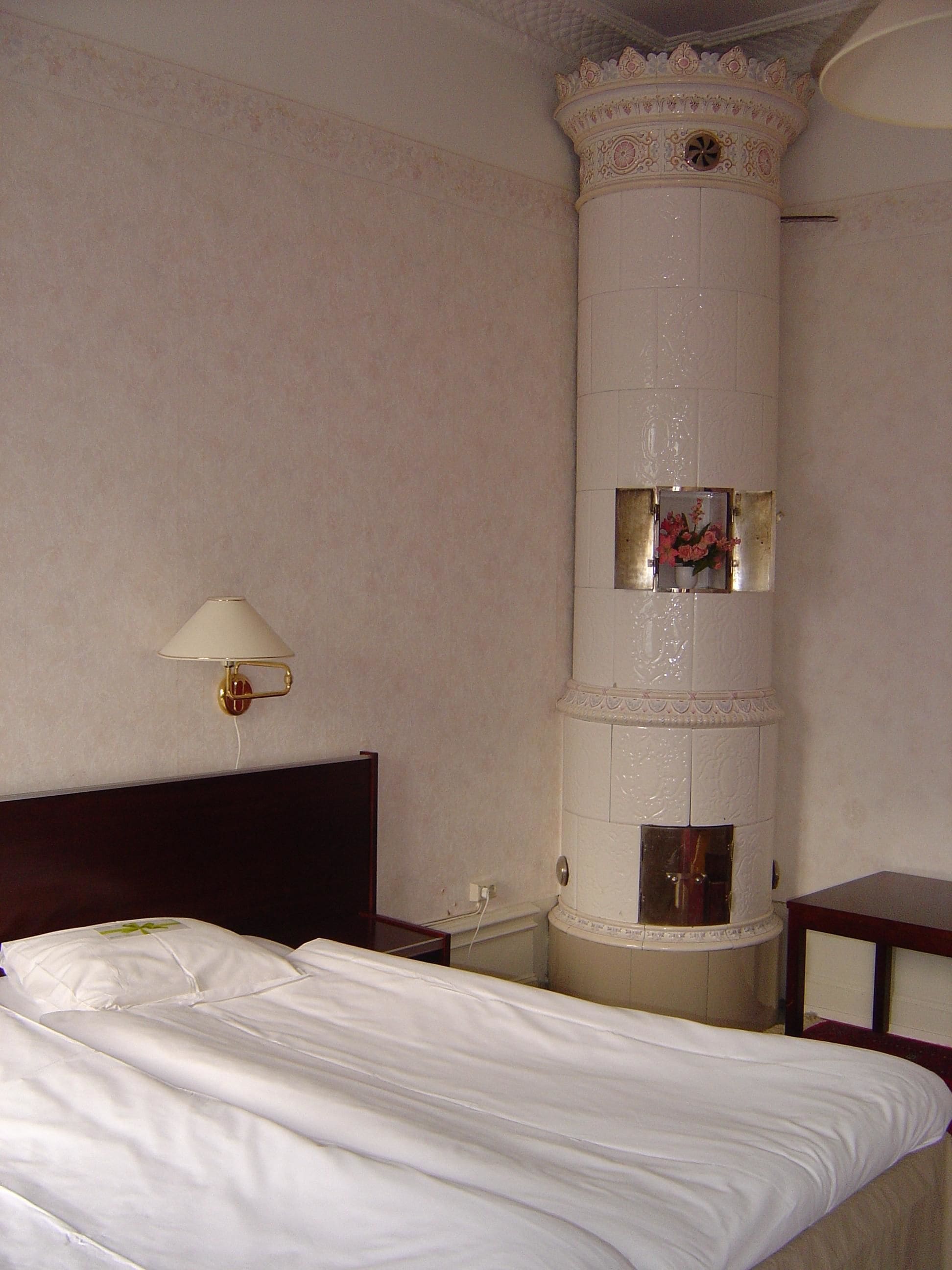 Una habitación de hotel con una cama, una mesita de noche, una lámpara y una columna decorativa.