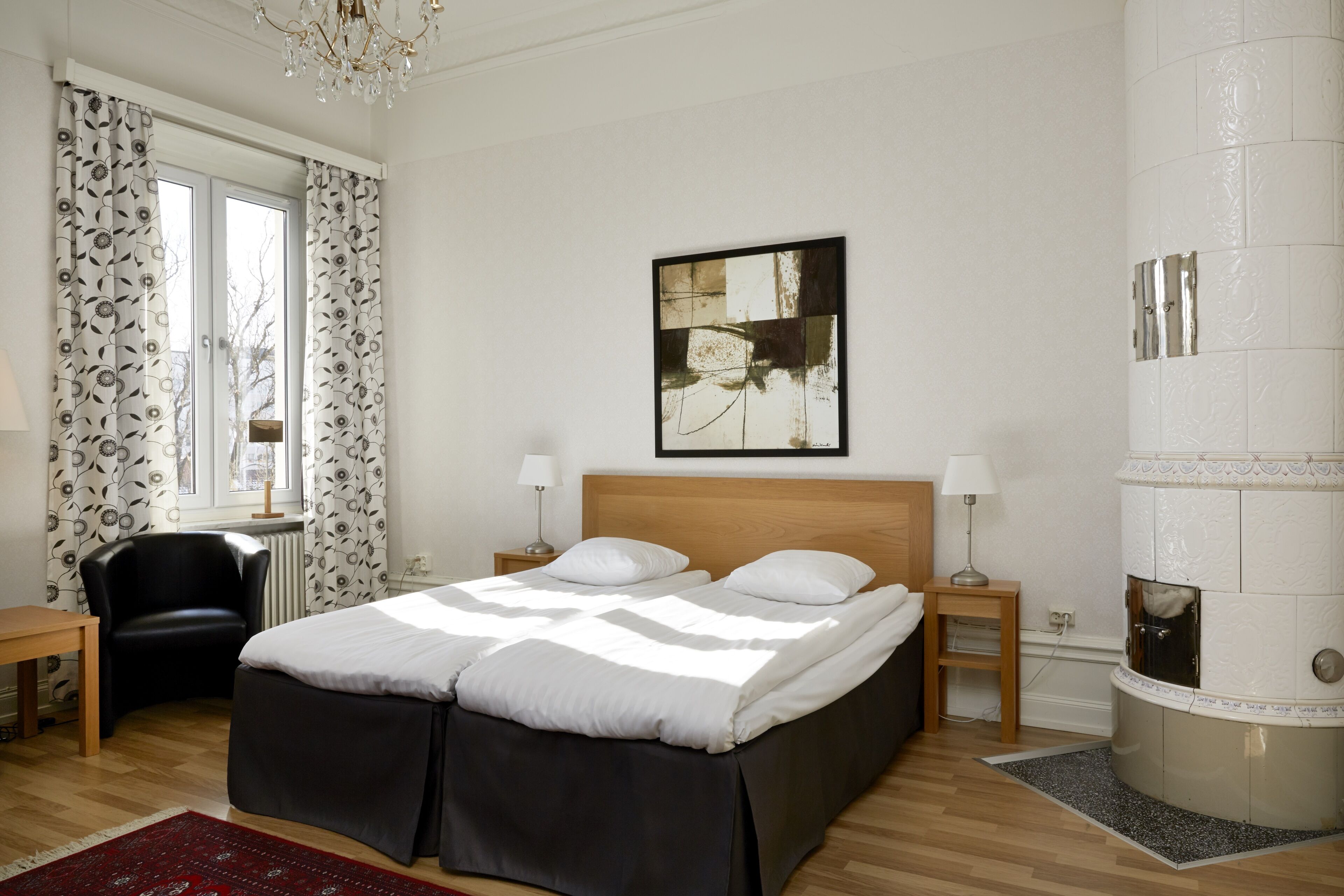 A bedroom with a bed, a chair, a small table, a lamp, and a fireplace.