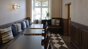 Een eetruimte met een geruit vloerkleed, een grote kroonluchter en een zithoek met tafels en banken.