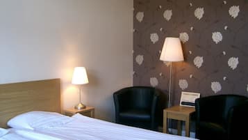 Ett hotellrum med en säng, två stolar, ett nattduksbord med en lampa och en vägg med ett blommönster.