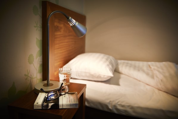 A neatly made bed with white linens, a bedside table with a lamp, a glass of water, and a book. - First Hotel City Eskilstuna (Eskilstuna)