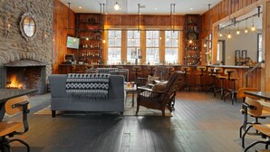 A cozy interior with a stone wall, wooden paneling, a fireplace, a bar area, and seating. - Mad River Barn (Waitsfield)