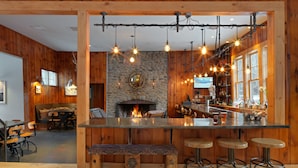 A rustic bar area with a stone fireplace, wooden beams, and a bar counter with stools. - Mad River Barn (Waitsfield)
