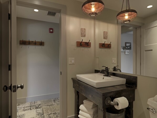 Un baño con lavamanos blanco, tocador de madera oscura y dos lámparas colgantes.