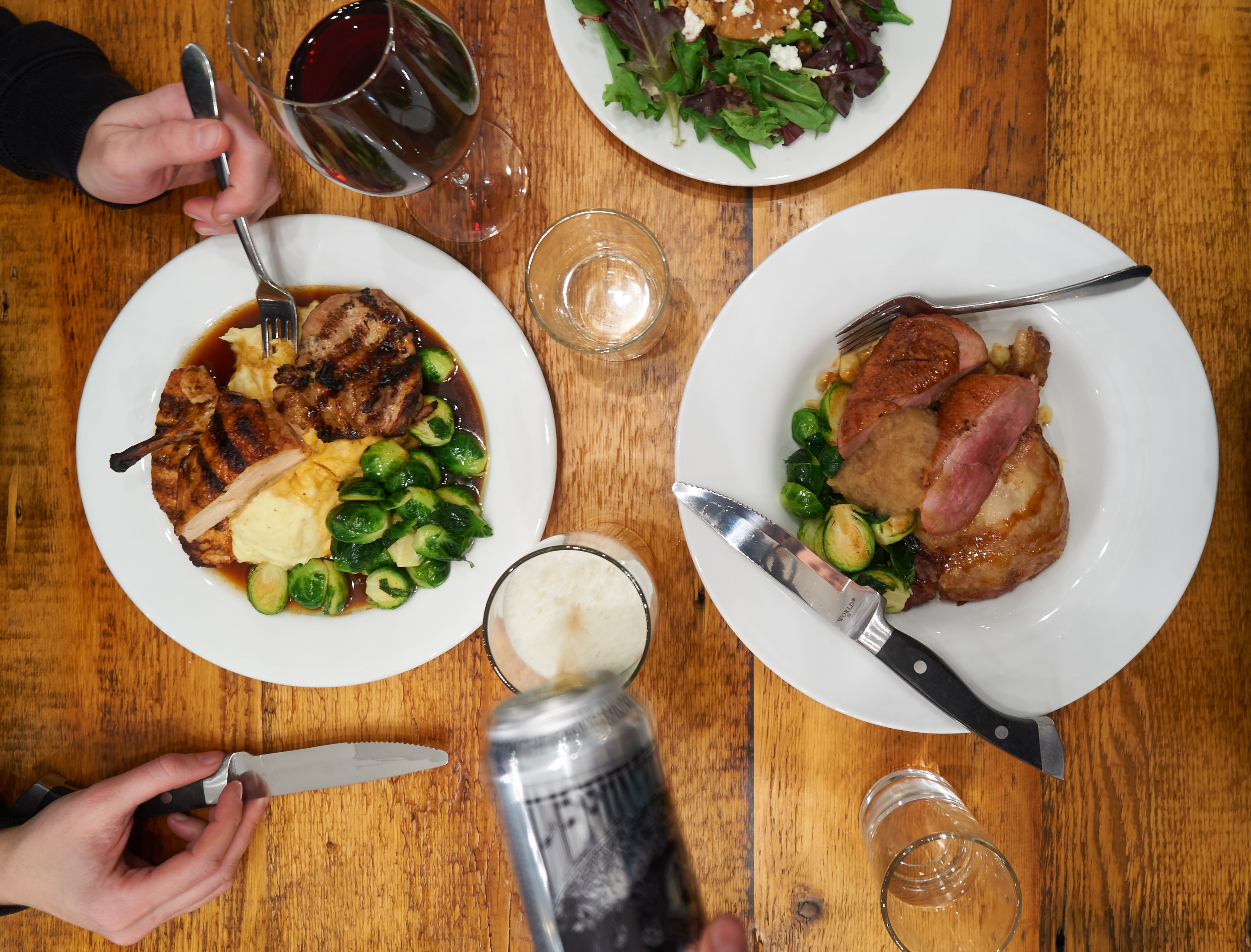 Two plates of food with a knife and fork on a wooden table.