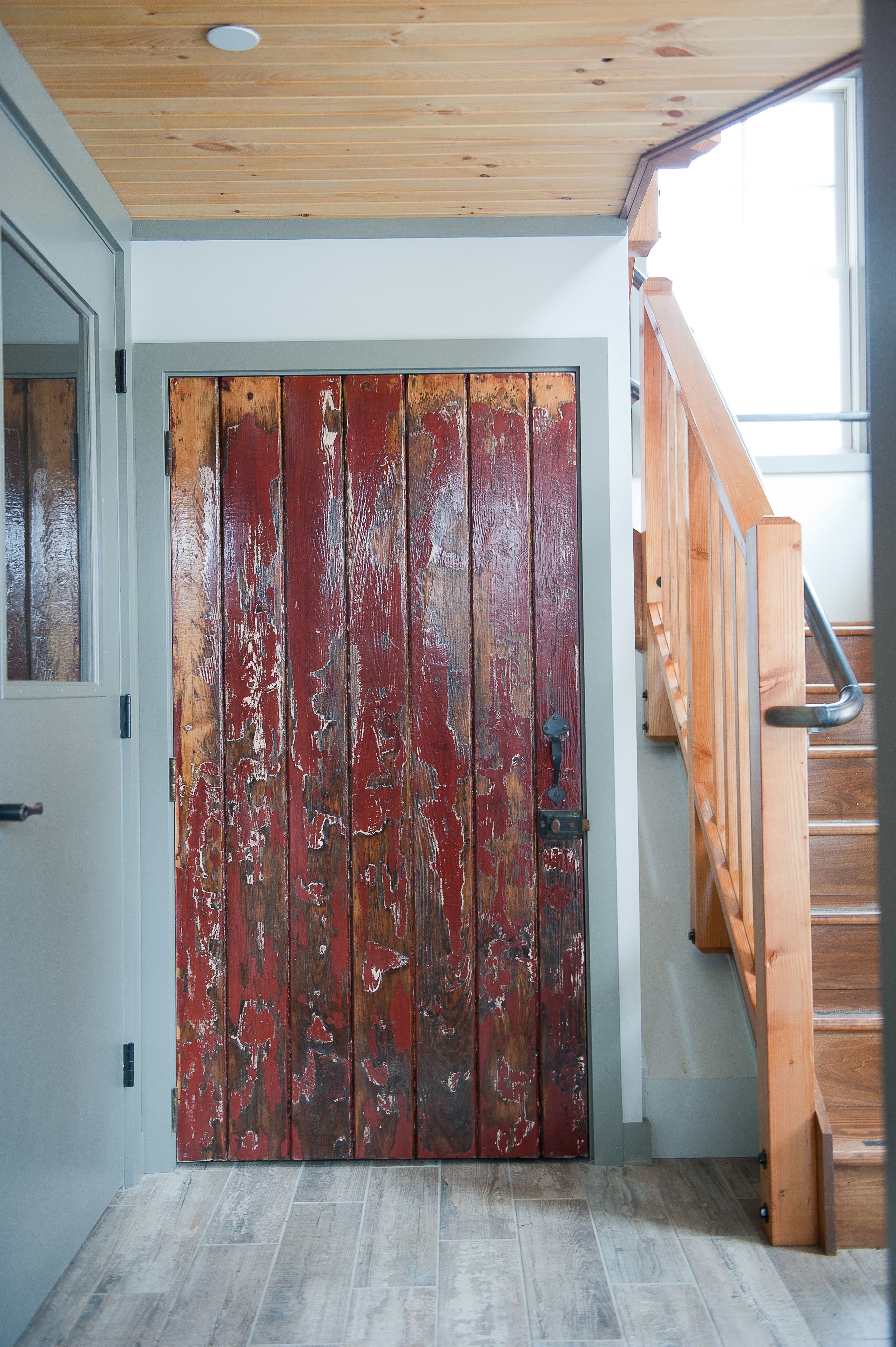 A wooden staircase with a metal handrail leading to a room with a white door featuring peeling red paint.