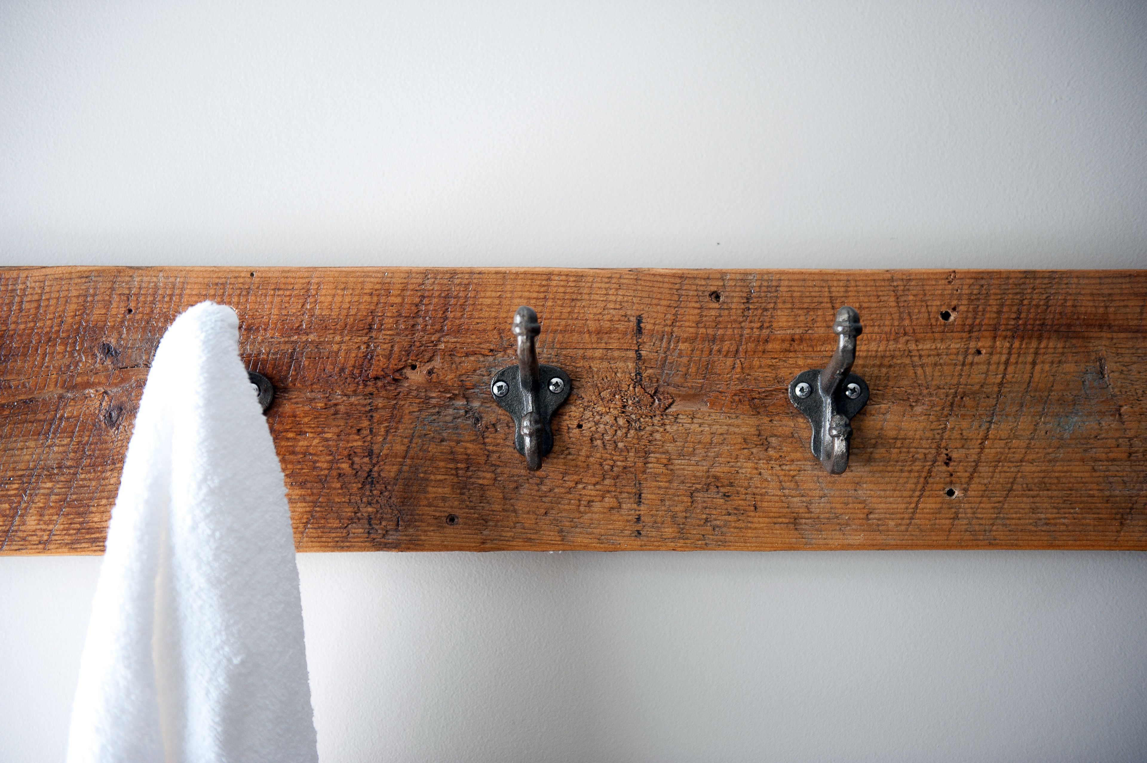 A wooden beam with two metal hooks and a white towel hanging from one of them.