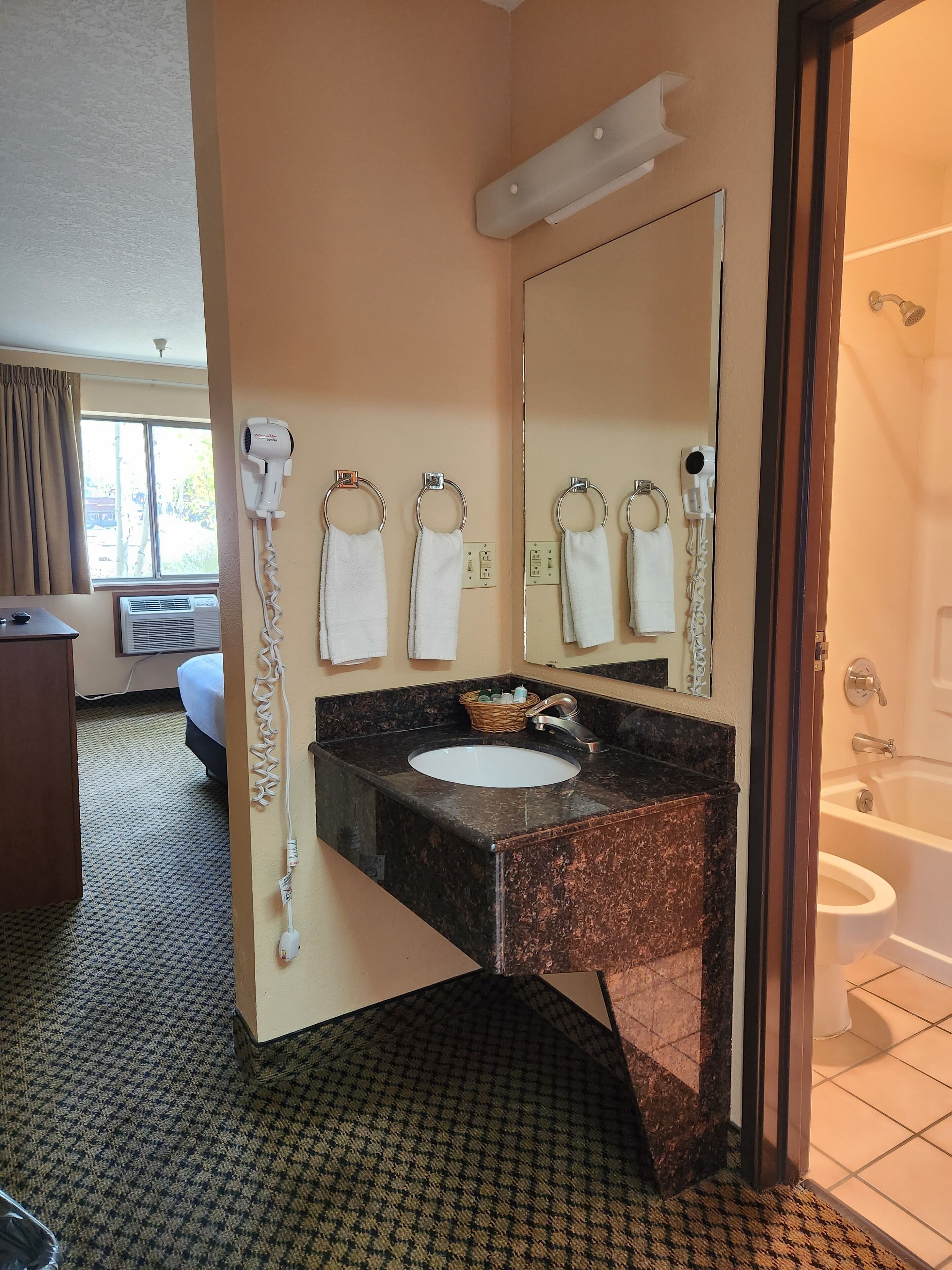 A hotel bathroom with a sink, mirror, towel rings, and a shower.