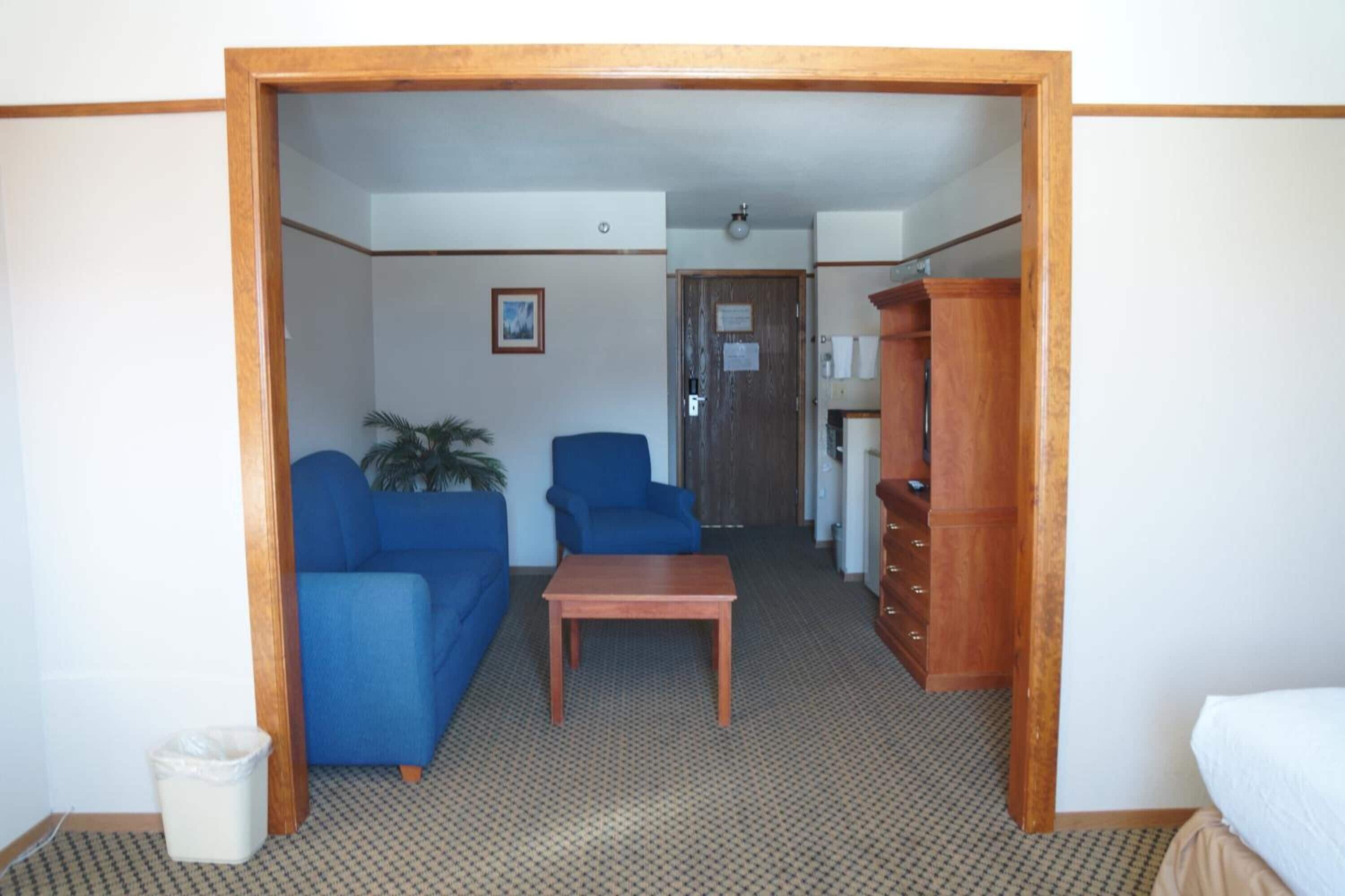 Una habitación de hotel con un sofá azul, una mesa de madera y un armario.