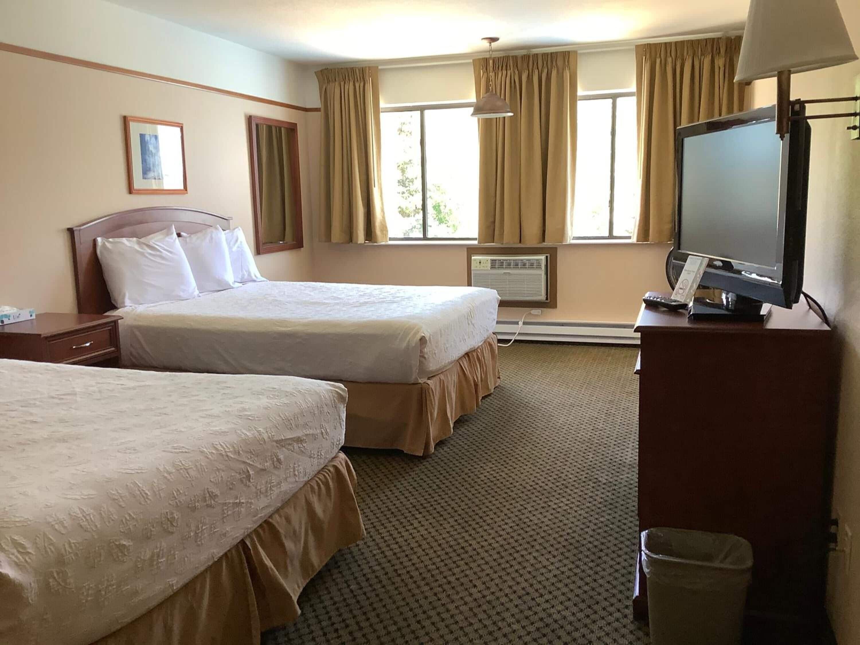 A hotel room with two beds, a television, a desk, and a window with curtains.