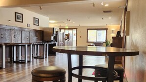 A spacious hotel lobby with a wooden floor, a reception desk, and a seating area with stools and a table.