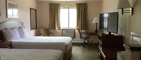 A hotel room with two beds, a desk with a television, a chair, and a desk lamp.