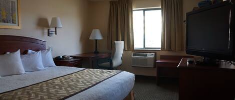 Habitación de hotel con una cama grande, un escritorio, una silla, un televisor y una ventana con cortinas.