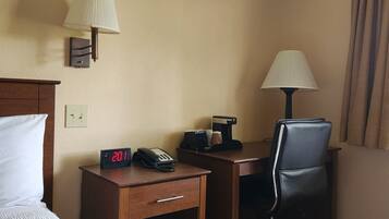 Une chambre d’hôtel comprenant un lit, un bureau avec une lampe, une chaise, une horloge et une machine à café.